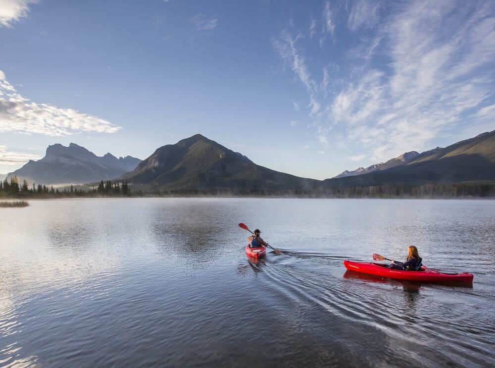 Two people in kayaks paddling on Vermilion Lakes at sunrise